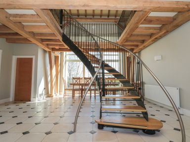 A room with a curved staircase wooden beams a dining table and chairs on tiled floor at The Barn Helperby near Boroughbridge