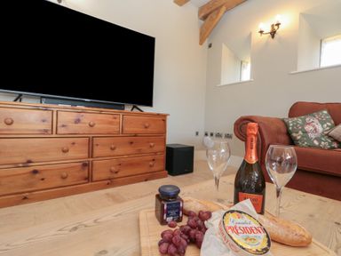 A living room with a wooden dresser a sofa with decorative cushions and a table with a bottle of wine cheese grapes and bread at The Barn Helperby near Boroughbridge