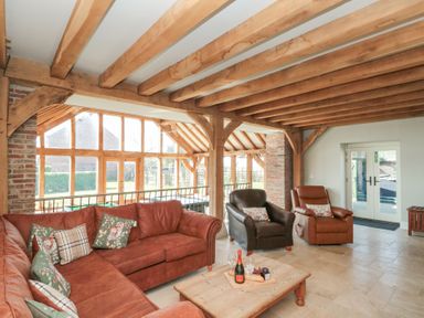 A living room with wooden beams a sectional sofa armchairs coffee table and large windows at The Barn Helperby near Boroughbridge