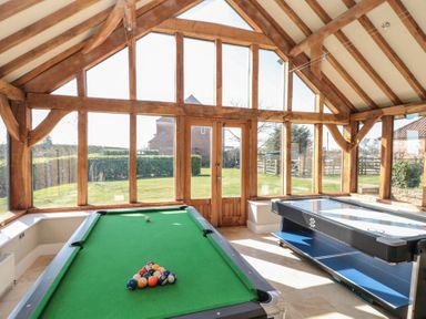 A game room with a pool table and an air hockey table in a glass enclosed space at The Barn in Helperby near Boroughbridge