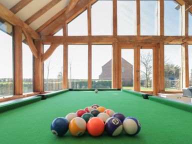 A billiard table with balls arranged inside a room with large windows and wooden beams at The Barn Helperby near Boroughbridge