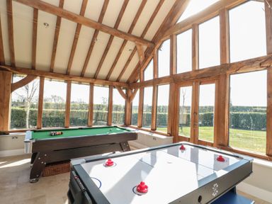 A game room with a pool table and an air hockey table with large windows and wooden beams at The Barn Helperby near Boroughbridge
