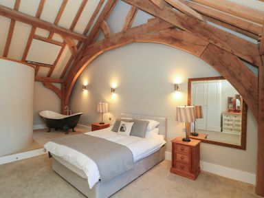 A bedroom with exposed wooden beams a bed with bedside tables and lamps a mirror and a clawfoot bathtub at The Barn Helperby near Boroughbridge
