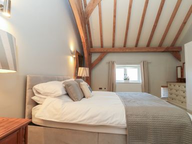 A bedroom with a bed pillows bedside table lamp window with curtains and wooden beams on the ceiling at The Barn Helperby near Boroughbridge