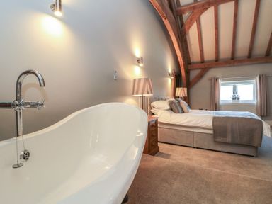 A bedroom with a freestanding bathtub wooden beams and a window at The Barn in Helperby near Boroughbridge