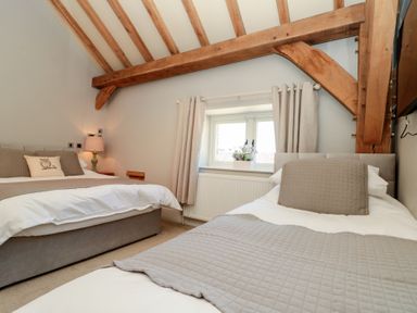 A bedroom with two beds, a window with curtains, and exposed wooden ceiling beams at The Barn Helperby near Boroughbridge