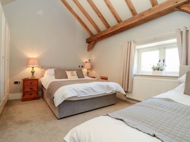 A bedroom with two beds wooden ceiling beams and a window with flowers at The Barn Helperby near Boroughbridge