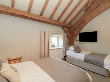 A bedroom with two beds a window with curtains wooden beams on the ceiling and a wall-mounted TV at The Barn Helperby near Boroughbridge
