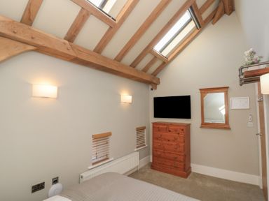 A bedroom with exposed wooden beams a wooden dresser a wall-mounted television and a mirror at The Barn Helperby near Boroughbridge
