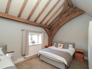 A bedroom with a double bed wooden bedside tables exposed timber beams and a window with curtains at The Barn Helperby near Boroughbridge