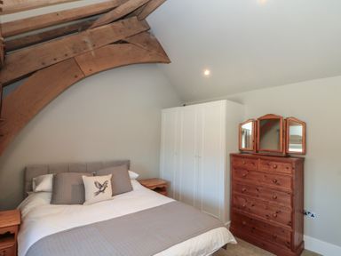 A bedroom with a bed pillows wooden side tables wardrobe and wooden dresser with mirror at The Barn Helperby near Boroughbridge