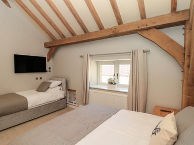 A bedroom with two beds a wall mounted television and wooden ceiling beams at The Barn in Helperby near Boroughbridge