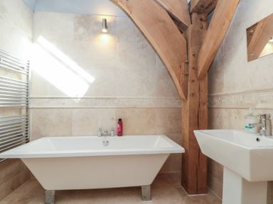 A bathroom with a bathtub a sink wooden beams and tiled walls at The Barn Helperby near Boroughbridge