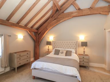A bedroom with a bed flanked by two bedside tables and lamps under exposed wooden beams at The Barn Helperby near Boroughbridge