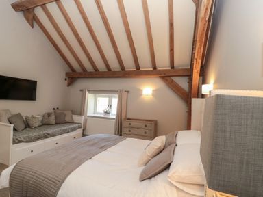 A bedroom with wooden beams a large bed a daybed a chest of drawers and a wall-mounted television at The Barn Helperby near Boroughbridge
