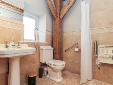 A bathroom with a pedestal sink and toilet next to a wooden beam and shower area at The Barn in Helperby near Boroughbridge