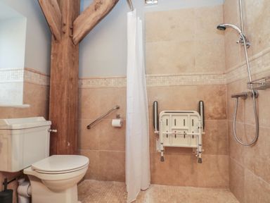 A bathroom with a toilet a shower area with a foldable seat and a wooden beam at The Barn Helperby near Boroughbridge
