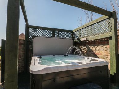 An outdoor hot tub with water jets surrounded by wooden lattice panels and a brick wall at The Barn in Helperby near Boroughbridge