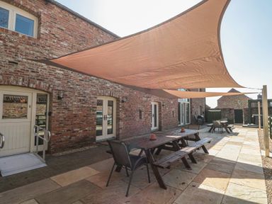 An outdoor patio with picnic tables and chairs under shade sails at The Barn in Helperby near Boroughbridge