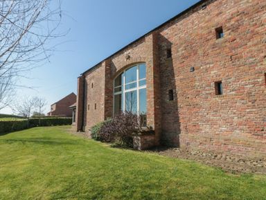 Exterior view of a brick building with arched window and surrounding green lawn at The Barn Helperby near Boroughbridge