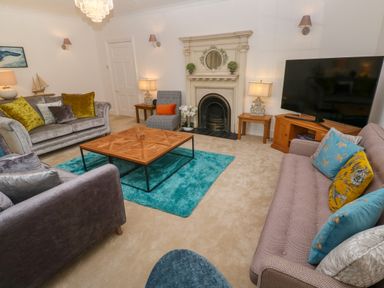 A living room with sofas a wooden coffee table a fireplace a large television and lamps at Hindon Hall in Lelant near Carbis Bay