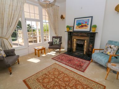 A living room with armchairs rugs a fireplace and large windows at Hindon Hall in Lelant near Carbis Bay