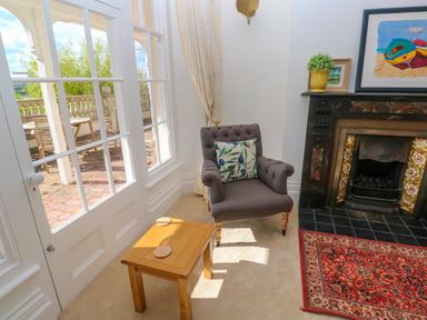 A sitting area with a gray armchair cushion wooden table fireplace and glass doors opening to a patio at Hindon Hall in Lelant near Carbis Bay