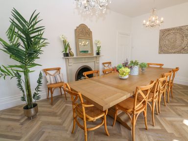 A dining room with a wooden table and chairs a potted plant a fireplace with a mirror and flowers and chandeliers at Hindon Hall in Lelant near Carbis Bay