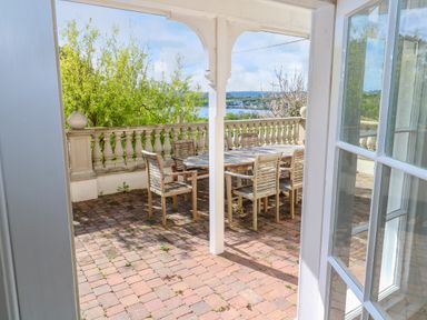 A patio with a wooden table and six chairs surrounded by a balustrade with a view of trees and water at Hindon Hall in Lelant near Carbis Bay