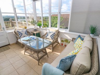 A sunroom with wicker furniture cushions and plants at Hindon Hall in Lelant near Carbis Bay