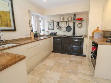 A kitchen with beige cabinets brown countertops a black stove pots pans and cooking utensils on the wall at Hindon Hall in Lelant near Carbis Bay