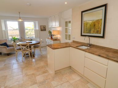 A kitchen with a round dining table and chairs near windows and a countertop with a sink and framed artwork on the wall at Hindon Hall in Lelant near Carbis Bay