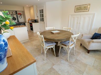 A dining area with a round wooden table and four chairs next to a kitchen and an armchair at Hindon Hall in Lelant near Carbis Bay
