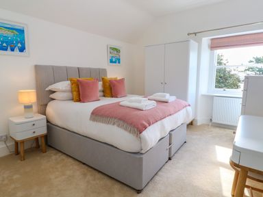 A bedroom with a bed pillows and folded towels a nightstand with a lamp a wardrobe a window and paintings at Hindon Hall in Lelant near Carbis Bay