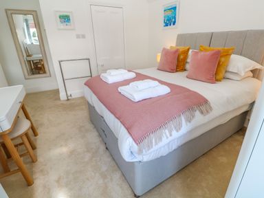 A bedroom with a bed with folded towels on it a small desk with a chair a full length mirror and two framed pictures on the wall at Hindon Hall in Lelant near Carbis Bay