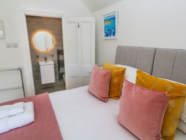 A bedroom with a bed with pink and yellow pillows and a bathroom with a round mirror at Hindon Hall in Lelant near Carbis Bay