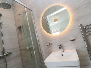 A bathroom with a glass shower enclosure a round illuminated mirror and a sink at Hindon Hall in Lelant near Carbis Bay