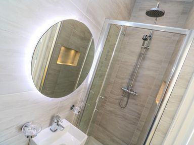 A bathroom with a circular mirror above a sink and a glass-enclosed shower with a rainfall showerhead at Hindon Hall in Lelant near Carbis Bay