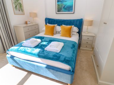 A bedroom with a blue bed frame white bedding yellow pillows two bedside tables with lamps and a dresser at Hindon Hall in Lelant near Carbis Bay