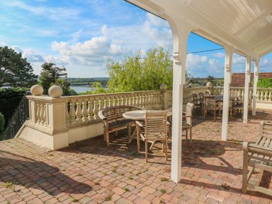 An outdoor patio with wooden tables and chairs under a white covered area and a balustrade overlooking greenery and water at Hindon Hall in Lelant near Carbis Bay