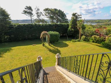 A garden with grass lawn and trees viewed from stone steps with black metal railings at Hindon Hall in Lelant near Carbis Bay