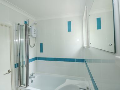 A bathroom with a bathtub shower and tiled walls with blue accents at The Beach Hut in Cromer