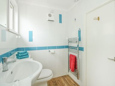 A bathroom with a sink, toilet, towel rack with a red towel, blue and white tiled walls at The Beach Hut in Cromer