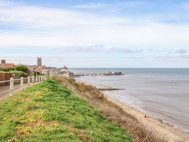 A coastal town with a church tower and pier viewed from a grassy cliff path at The Beach Hut in Cromer