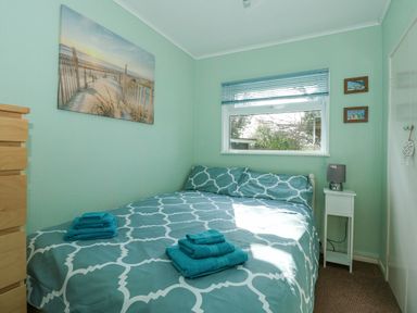 A bedroom with a bed with patterned bedding and folded towels beside a window at The Beach Hut in Cromer