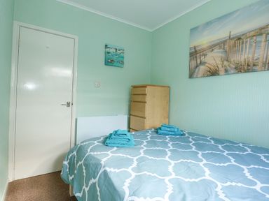 A bedroom with a bed covered in a patterned duvet and folded towels on top and a chest of drawers against the wall at The Beach Hut in Cromer