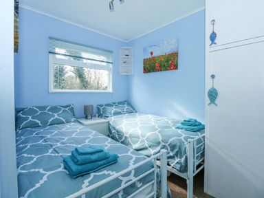 A small bedroom with two single beds a nightstand and a window at The Beach Hut in Cromer