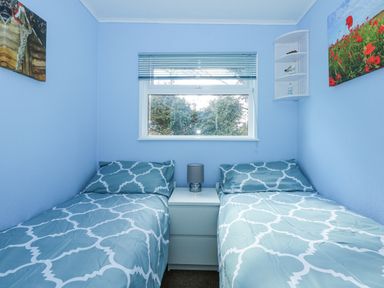 A bedroom with two single beds separated by a nightstand with a lamp and a window above at The Beach Hut in Cromer