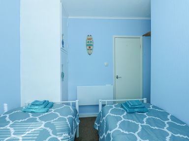 A bedroom with two single beds with patterned bedding and folded towels on top at The Beach Hut in Cromer