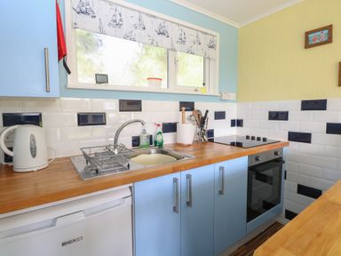 A kitchen with blue cabinets wooden countertops a white kettle a dish drying rack and an oven at The Beach Hut in Cromer